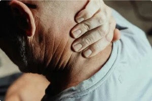 Elderly man holding his neck in pain, seeking online doctor consultation for relief