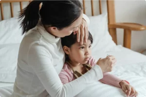 Mother checking her daughter’s temperature for fever, accessing online GP advice through DirectDoc